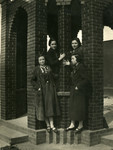 Four young women stand on the ledge of a brick structure under the bridge, in Salonika in 1940.